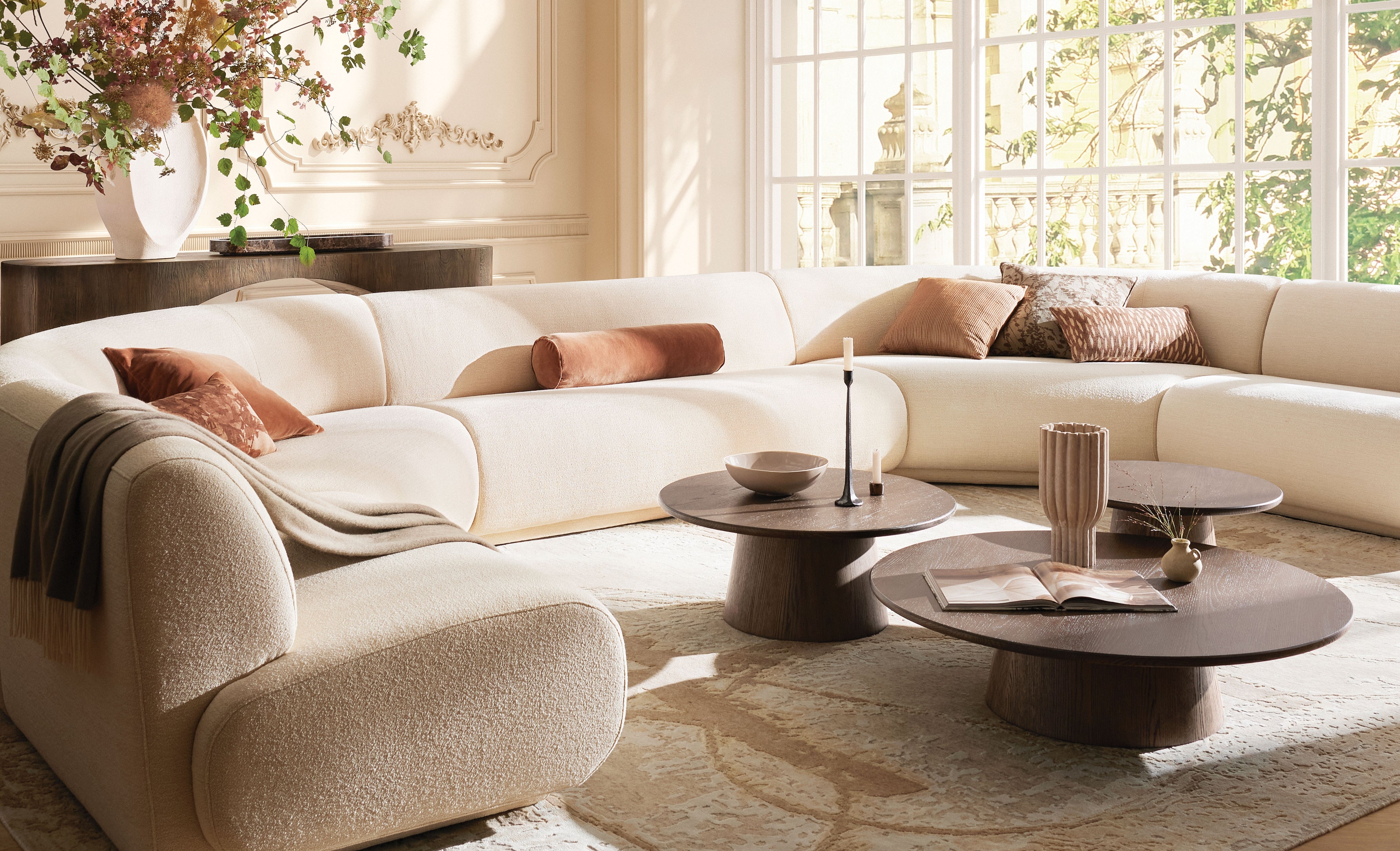 Modern living room with a white sectional sofa, wooden coffee tables, and decorative pillows.